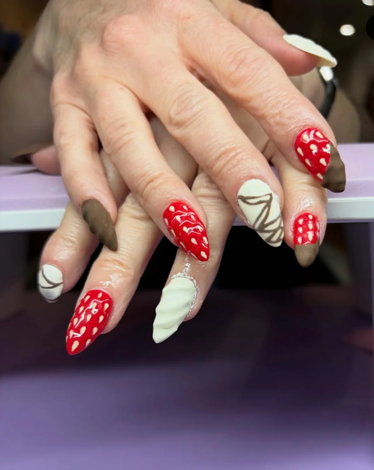 Long almond nails with red strawberry-inspired art and cream accents